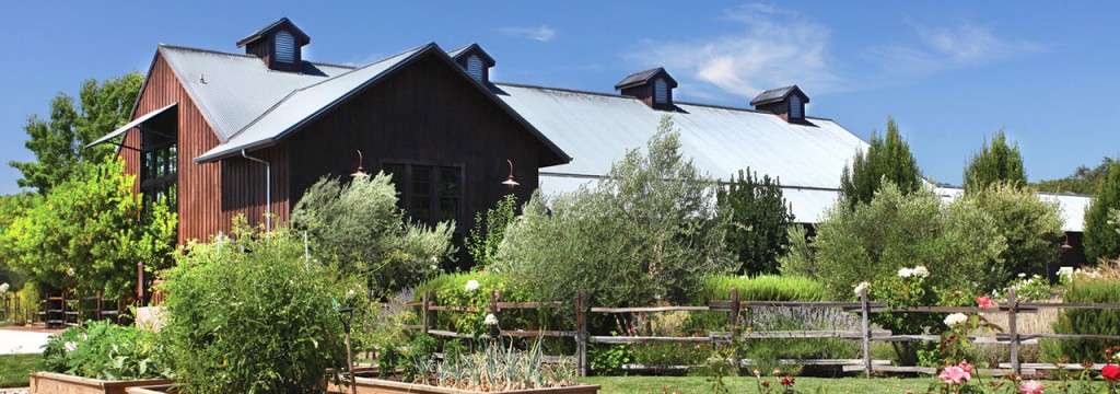 Red wood tasting room with a metal roof surrounded by beautiful green bushes and trees in spring.
