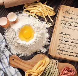 cracked egg in pile of flour with uncooked pasta noodles next to a cookbook