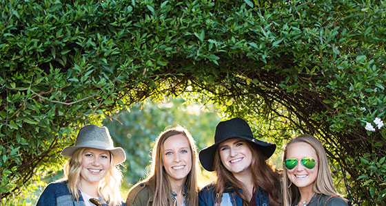 four women underneath a vine covered arch