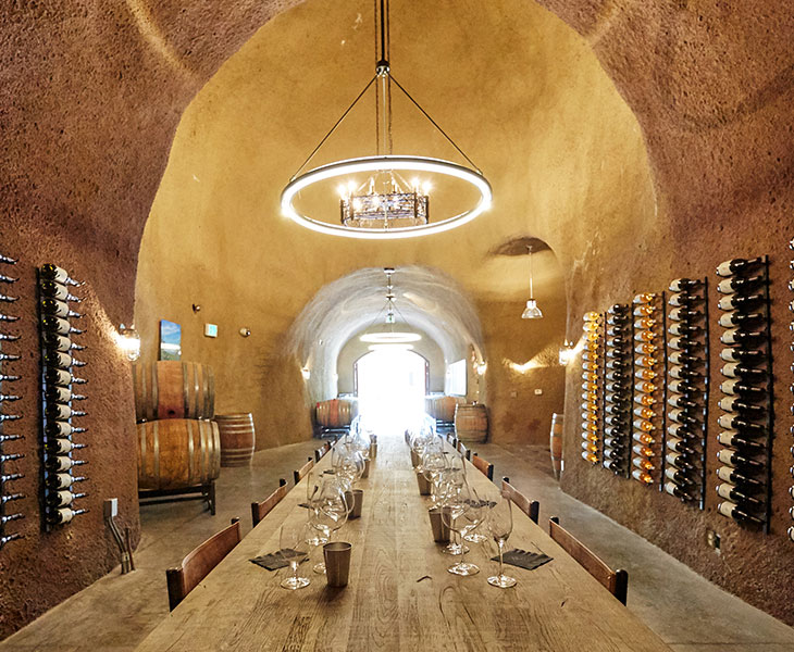 long dining table set for wine tasting in a wine cave with bottles of wine on the wall