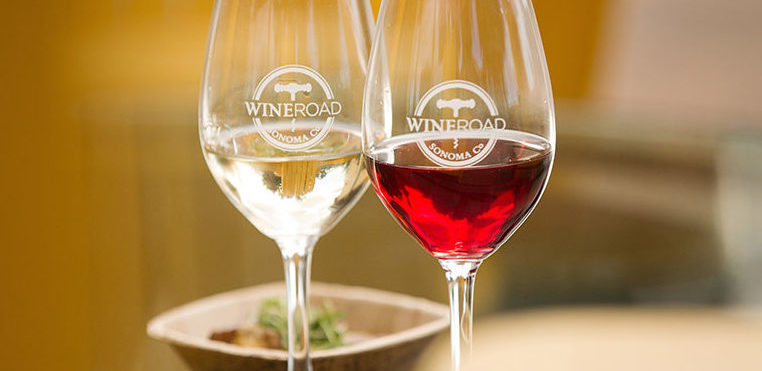 Two Wine Road logo'd glasses one with white wine one with red wine in front of a serving of food.