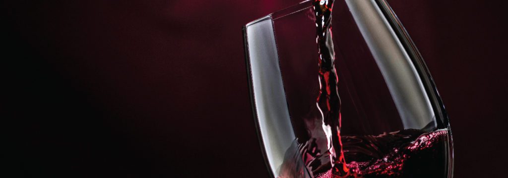 Red wine being poured into a glass with burgundy background.