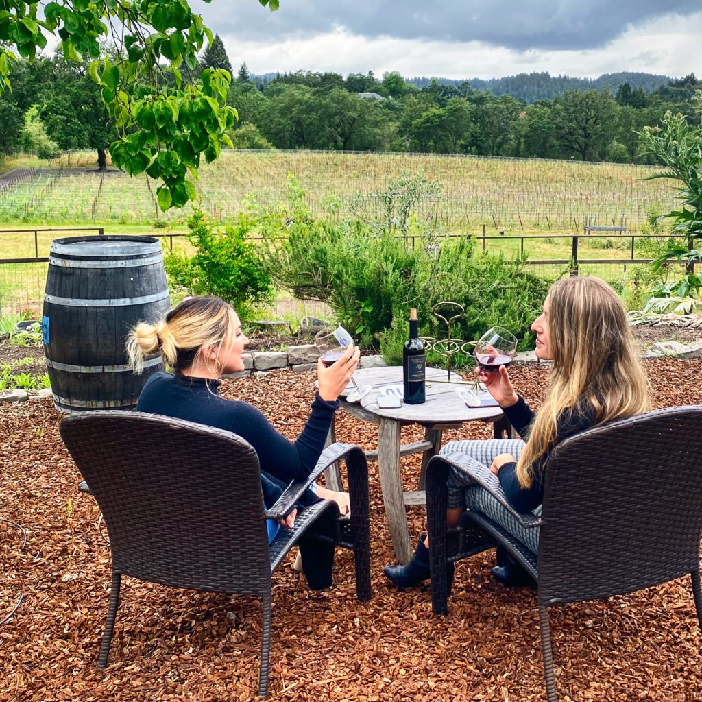 Two women enjoying a Russian River Vineyards red wine with views of the vineyard and the distant hills of Russian River.