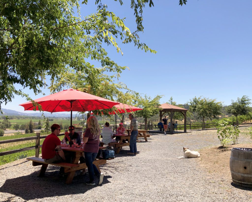 Picnic tables with red umbrellas filled with wine tasters at the garden area of J. Rickards Vineyards and Winery.