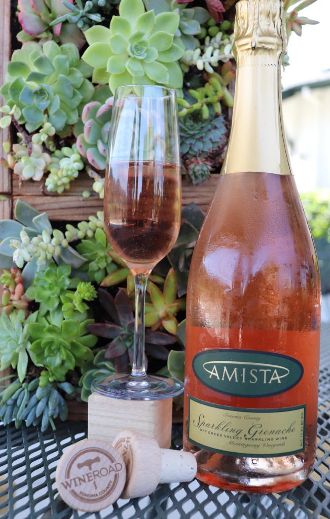 A glass and bottle of Amista's sparkling granache in front of a succulent planter.