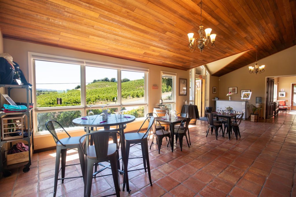 The tasting room of Pendroncelli with high top tables and chairs at the west window looking over their vineyards.