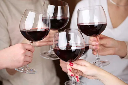 four large glasses filled with red wine, held by four people, but can only see their hands.