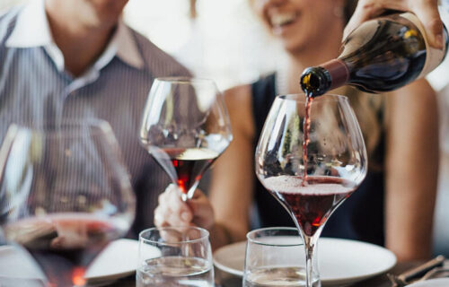 red wine being poured into glasses with a man and woman in the blurred background