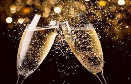 two champagne flute filled with bubbling champagne and toasting as bubbles splash around the glasses